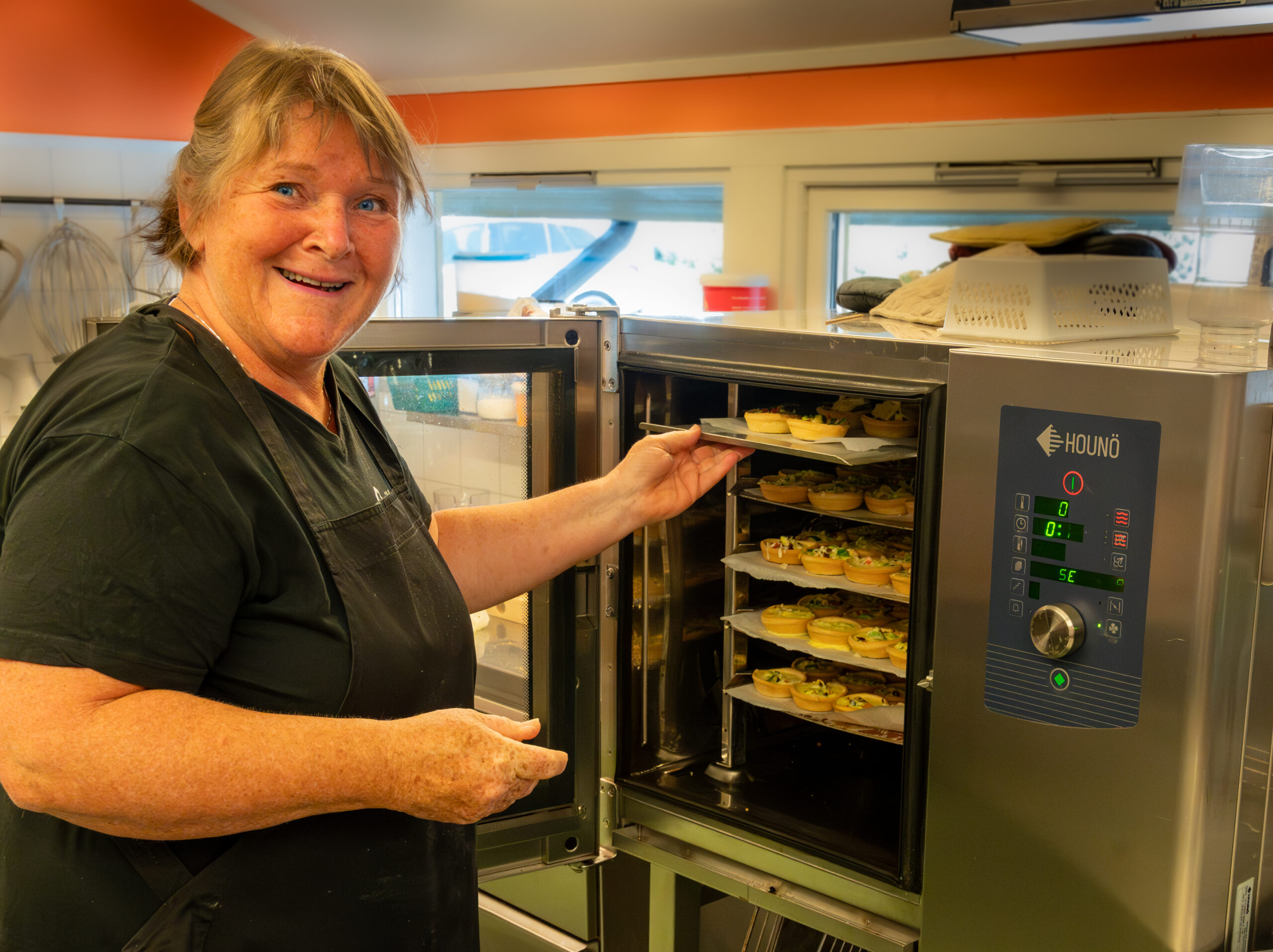 Turid står ved stekeovnen med brett med mat